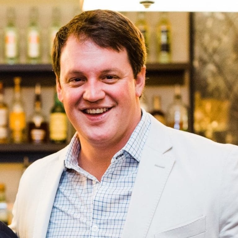 Man in a suit smiling in front of a bar